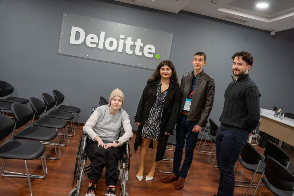 Three students and an industry expert, posing for a photograph, in a Deloitte training room