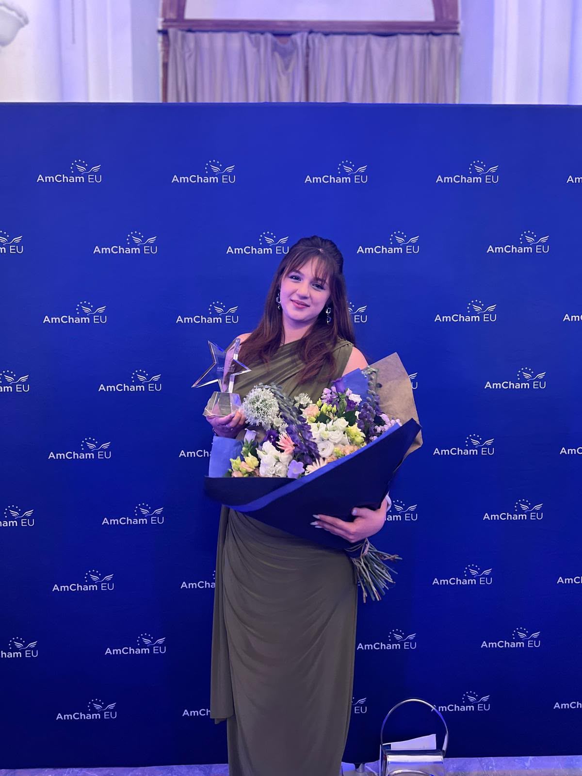 Elenya Spiteri holding a star trophy and bouquet of flowers at the AmCham EU awards ceremony